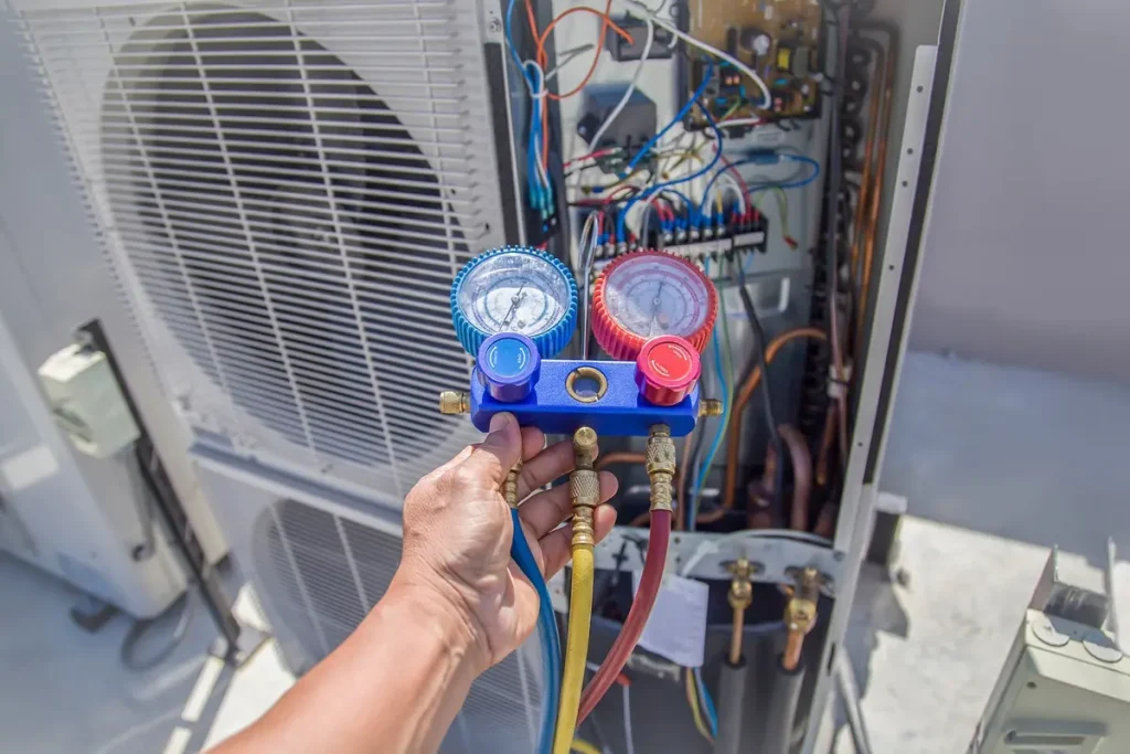 Man’s hand holding a device with red and blue gauges next to an open HVAC unit.