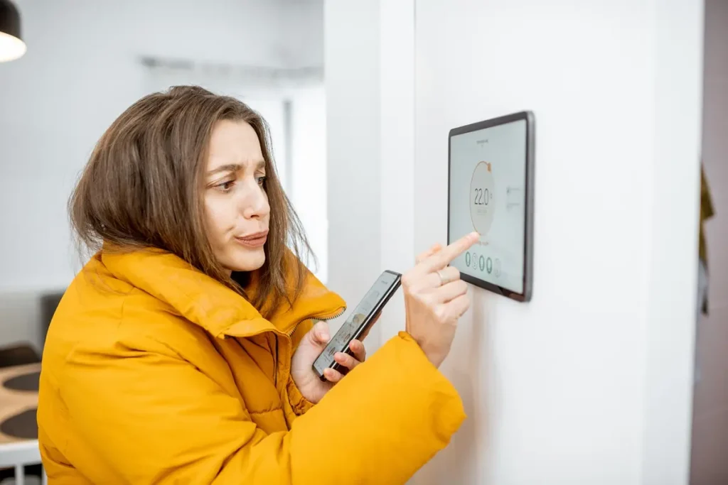 Young woman dressed in yellow winter jacket with a pointed finger on a digital tablet fixed on white wall and holding a smart phone in the other hand.