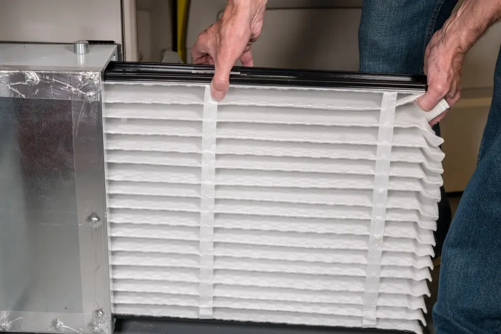 Close up of a man's hands holding an hvac filter that’s being slid into its casing.