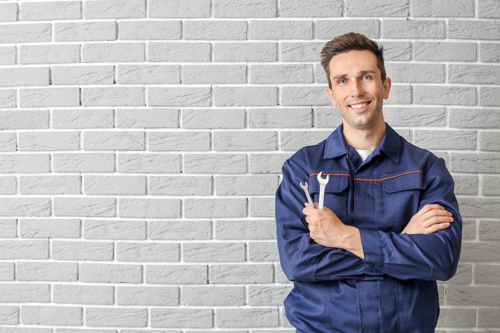 Male mechanic standing with hands crossed near brick wall with wrenches in hand