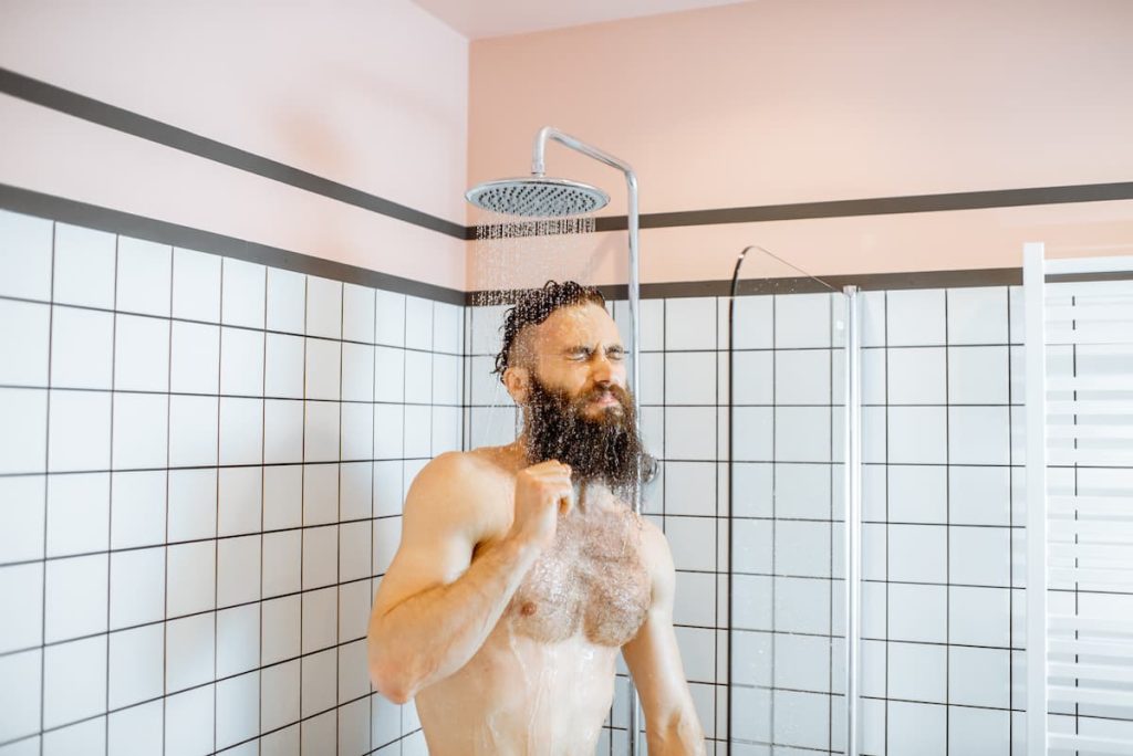 Man expressing shock from a cold shower as he stands under the showerhead
