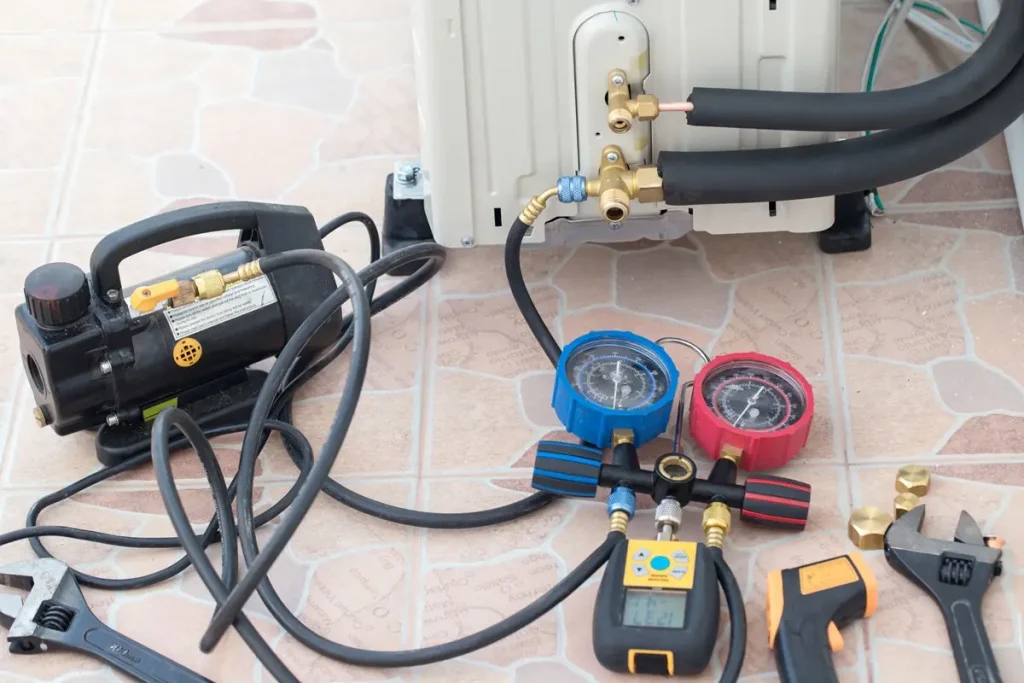 pump, gauges and wrenches sitting on tile floor next to an air conditioner unit.