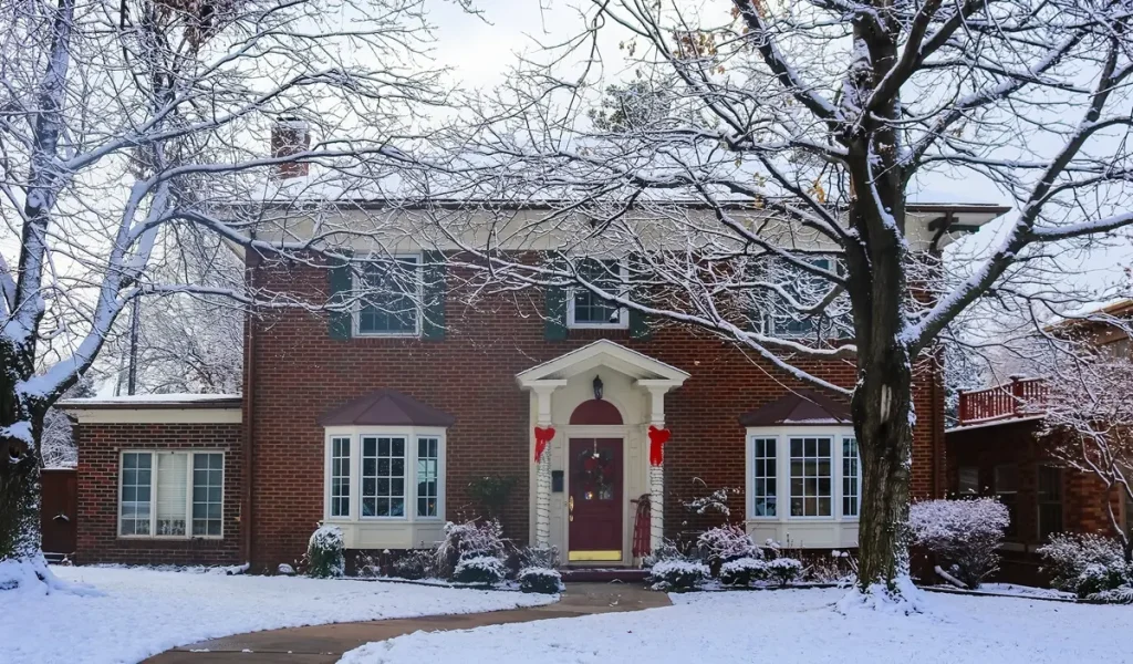 Snow covering the roof and lawn of a large brick house, adorned with Christmas decorations.